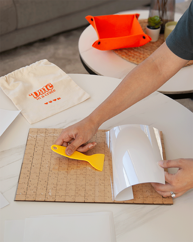 Applying puzzle glue sheets with scraper tool from Date in a Crate Puzzle Crate.
