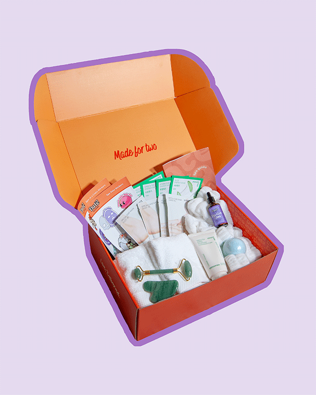 Angled view of Date in a Crate Spa Crate on a lavender background with a purple outline, featuring multiple Innisfree sheet face masks, hand and foot masks, a jade roller and gua sha, cotton white towels, a bottle of Relaxation Ritual massage oil, a blue ocean scented bath bomb, an Innisfree Green Tea Cleansing Foam and spa date stickers.