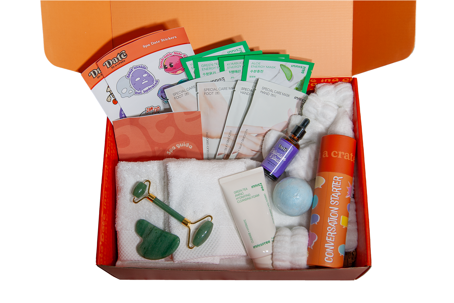 Open Date in a Crate Spa Crate box showing contents including spa-themed stickers, multiple sheet masks, face and foot masks, Innisfree green tea cleansing foam, jade roller and gua sha, blue bath bomb, fluffy headband, white towel, massage oil bottle, and conversation starter tube.