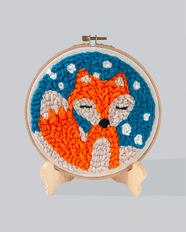 Embroidery hoop featuring an orange fox with eyes closed on a blue stitched background with white snow-like details.
