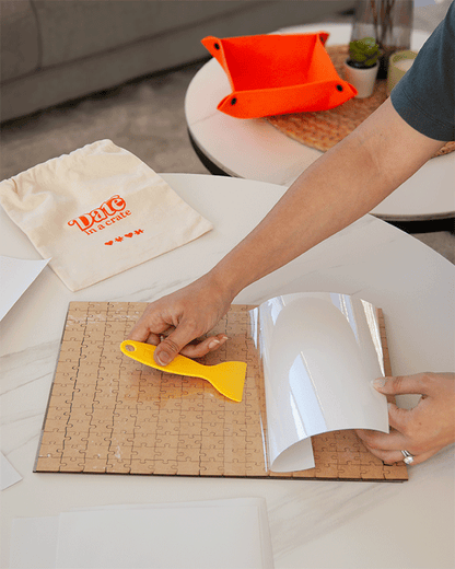 Applying puzzle glue sheets with scraper tool from Date in a Crate Puzzle Crate.