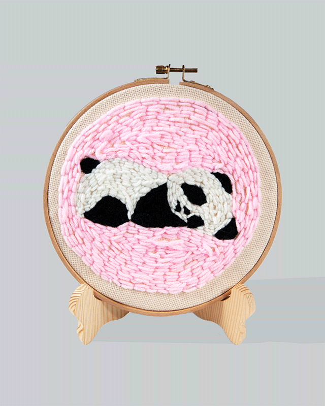 Embroidery hoop with a sleepy panda design on a pink stitched background.