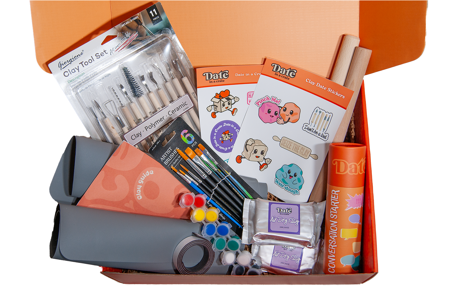 Open Date in a Crate Clay Crate showing included items: clay tool set, paintbrush set, paint pots, grey silicone clay mats, wooden rolling pins, two packs of 250g air dry clay, clay guide, fun illustrated clay-themed stickers, magnet tape and Conversation Starter game.