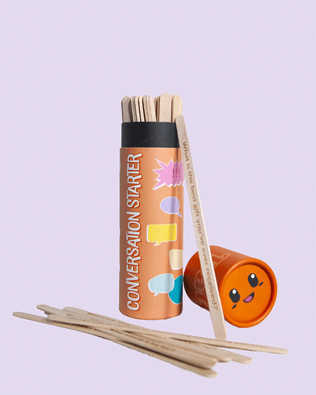 Conversation Starter game tube with orange lid open, showing wooden sticks inside with printed questions, one leaning against the tube and several spread on the surface, set on a light purple background.